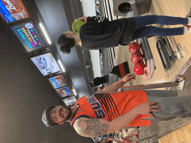 a man wearing an orange suns jersey stands in front of a woman bowling