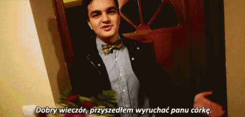 a man in a bow tie is standing in front of a door holding a bouquet of flowers