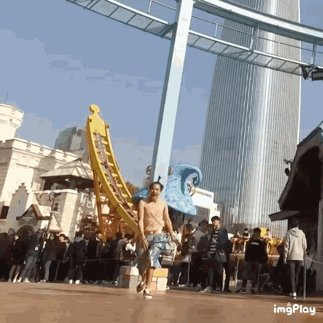 a man without a shirt is running in front of a roller coaster