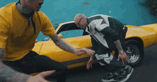 a man in a yellow shirt is kneeling down next to another man in a yellow car .