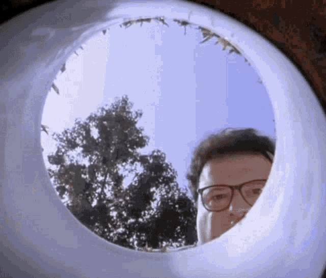 a man wearing glasses is looking through a hole in a pipe