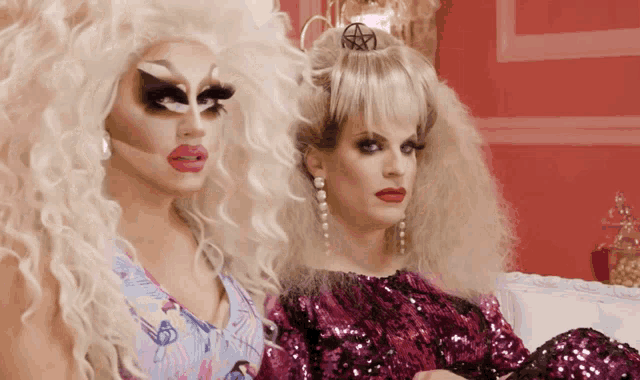 two drag queens sitting next to each other with one wearing a pentagram in her hair