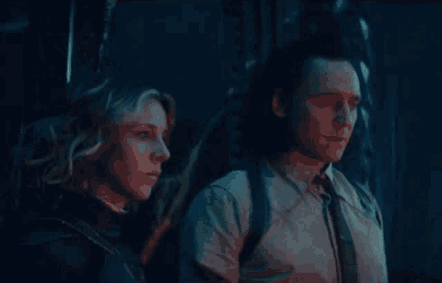 a man and a woman are standing next to each other in a dark room and looking at something .