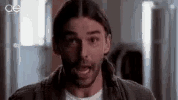 a man with long hair and a beard is making a funny face while standing in front of a window .