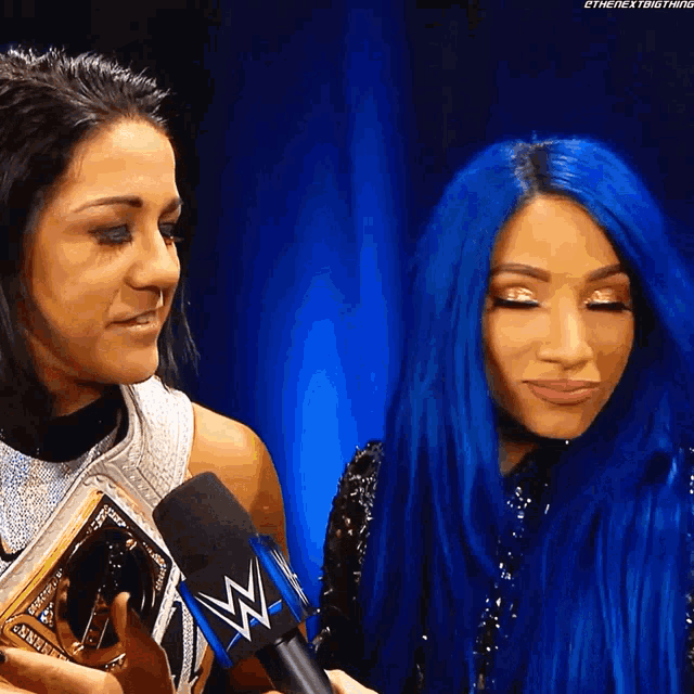 two women with blue hair are standing next to each other and one of them is wearing a wwe championship belt