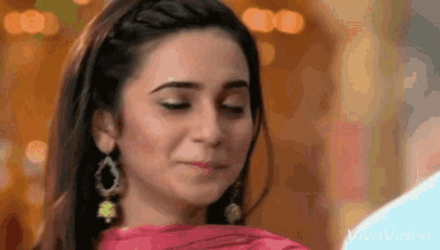 a close up of a woman wearing earrings and a pink dress making a funny face .