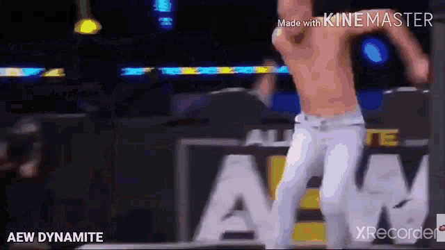 a man without a shirt is dancing on a stage in front of an aew dynamite sign .