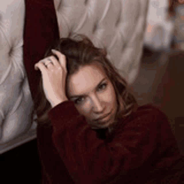a woman in a maroon sweater is laying on the floor with her hand on her head .