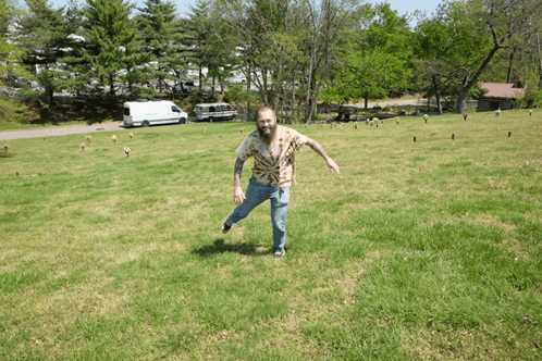 a man in a hawaiian shirt is standing in a grassy field