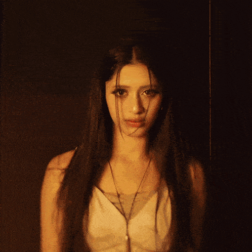 a woman with long hair and a necklace is standing in a dark room