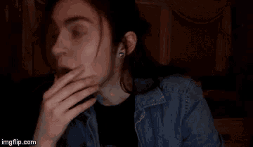 a man with long hair is yawning and covering his mouth with his hand in a dark room .
