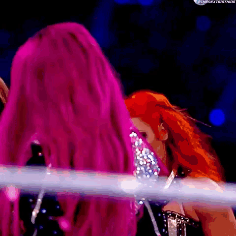 a woman with pink hair is standing next to another woman with red hair in a ring .