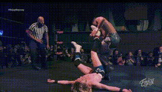 a wrestler is kneeling down in a wrestling ring while a referee looks on .