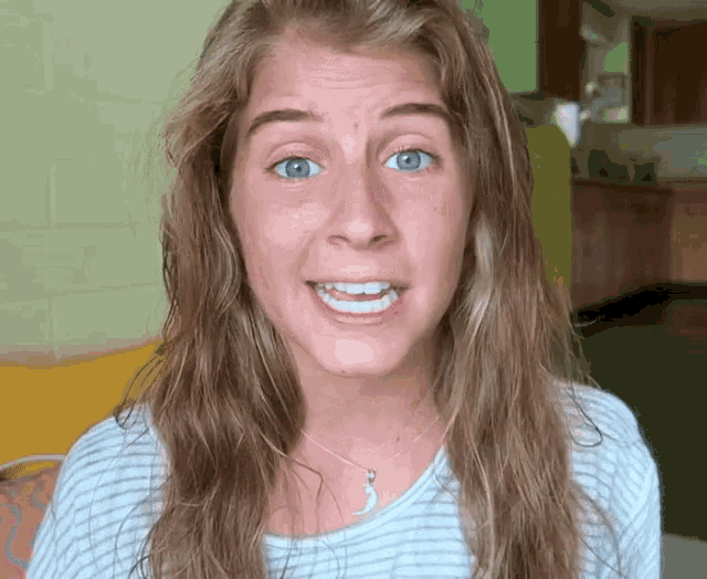 a woman with long hair and blue eyes is smiling and wearing a necklace