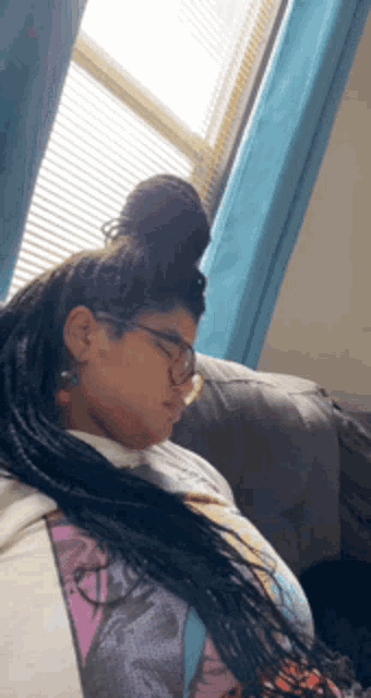 a woman with braids and glasses is sleeping on a couch