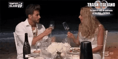 a man and a woman are sitting at a table with a bottle of wine and a sign that says trash italiano
