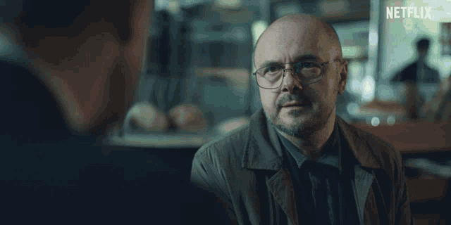 a bald man wearing glasses talks to another man with a netflix logo in the corner