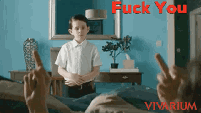 a boy in a white shirt stands in front of a blue wall with the words " fuck you " in red letters
