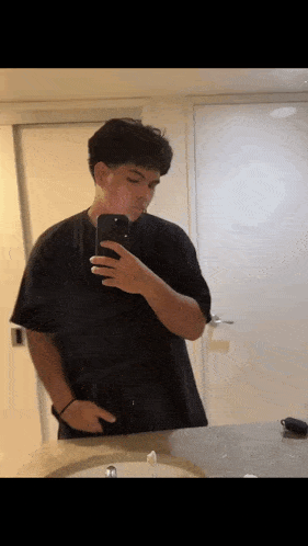a man in a black shirt is taking a selfie in front of a mirror .