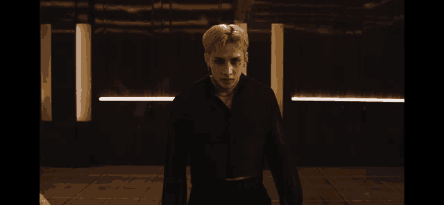 a man in a black shirt stands in a dark room with lights behind him