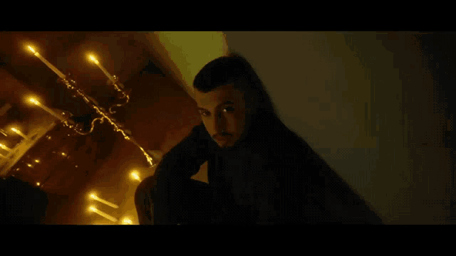 a man is sitting in a dark room with candles on the wall .