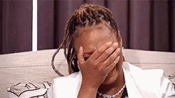 a woman with dreadlocks is covering her face with her hand .