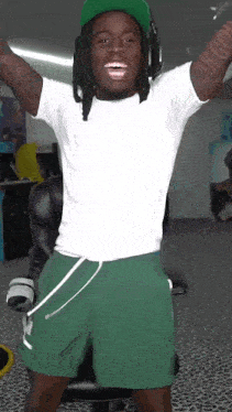 a man wearing a white shirt and green shorts is standing in a room with his arms in the air