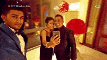 a man in a suit is taking a selfie with a woman and a man in a suit