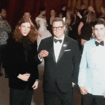 a man in a tuxedo is holding hands with two other men in tuxedos
