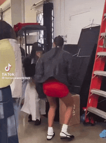 a woman in red shorts is dancing in a room with a ladder and boxes