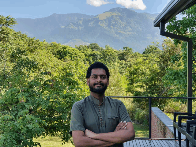 a man stands with his arms crossed in front of a mountain range