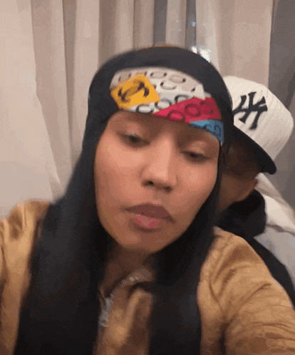 a woman wearing a head scarf and a ny hat looks at the camera