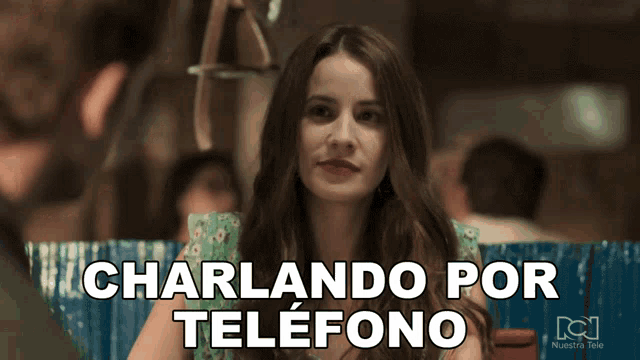 a woman is sitting in front of a sign that says charlando por telefono on it