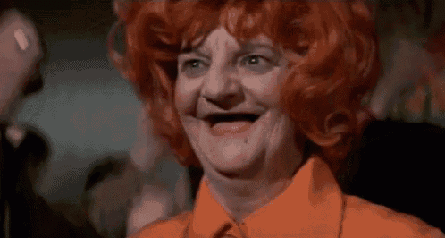 a woman with red hair and an orange shirt is smiling with a missing tooth .