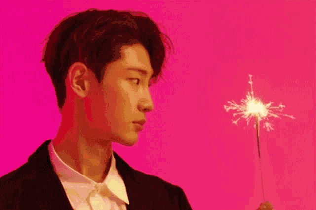 a young man in a suit and white shirt is holding a sparkler in his hand .
