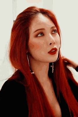 a woman with red hair is wearing hoop earrings and a black top