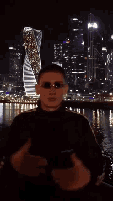 a man wearing sunglasses is standing in front of a building that says ' dubai ' on it