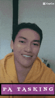 a man in a yellow hoodie is smiling in front of a purple sign that says pa tasking