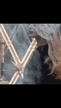 a woman with long blonde hair is standing in front of a glass dome with her hair blowing in the wind .