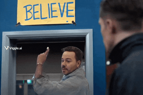 a man is pointing at a sign that says believe on it