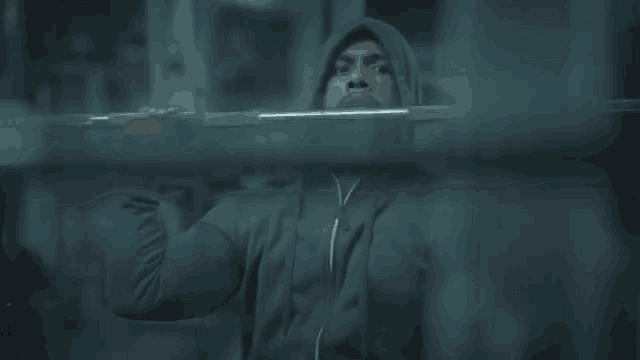 a man in a hooded jacket is squatting with a barbell in a gym .