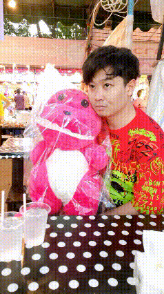 a man in a red shirt holds a pink stuffed animal on a table