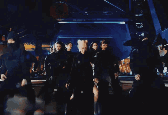 a group of people are dancing in a dark room with a blue light behind them