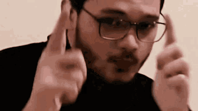 a man wearing glasses and a black shirt is making a funny face and pointing at the camera .