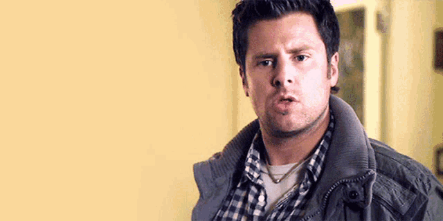 a man wearing a plaid shirt and a jacket is making a face .