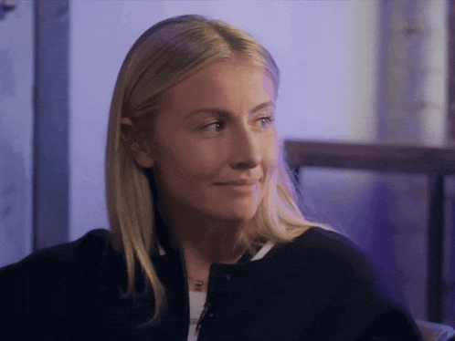 a woman with blonde hair is wearing a black jacket and a necklace with a dog on it