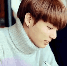 a young man wearing a turtleneck sweater and earrings is smiling .