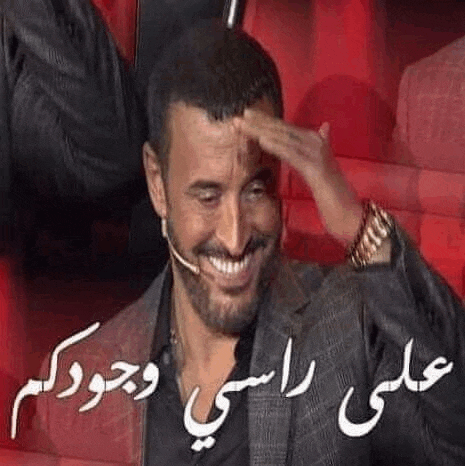 a man in a suit is sitting in a red chair with his hand on his forehead and smiling .