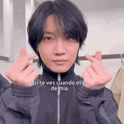 a man in a black jacket making a heart shape with his fingers