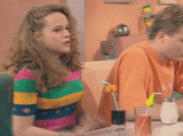 a woman in a striped shirt sits at a table with a man in an orange shirt